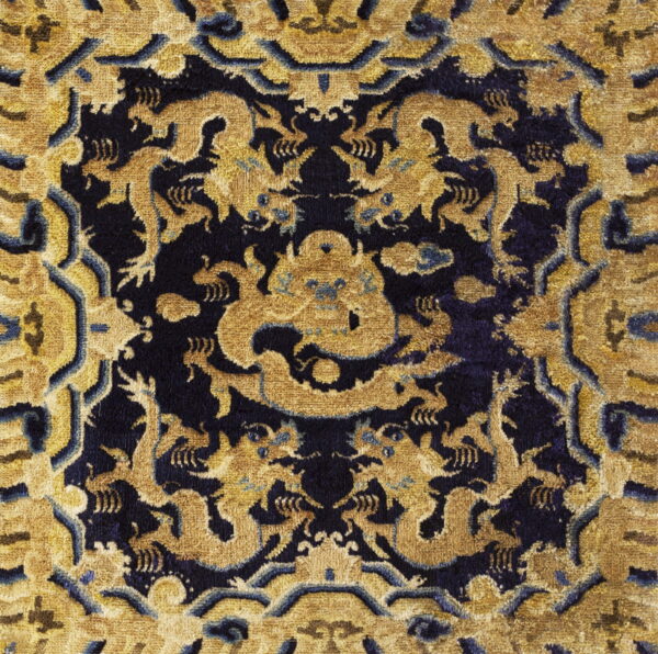 Intricate gold and dark blue rug with a symmetrical pattern of stylized dragons and figures.