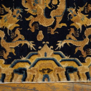 Intricate high-pile rug featuring gold and teal mythological creatures on a dark blue field over wood flooring.