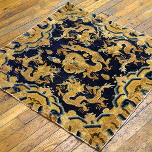 Low-pile square rug featuring gold dragons on a dark blue ground, set on aged wood flooring.
