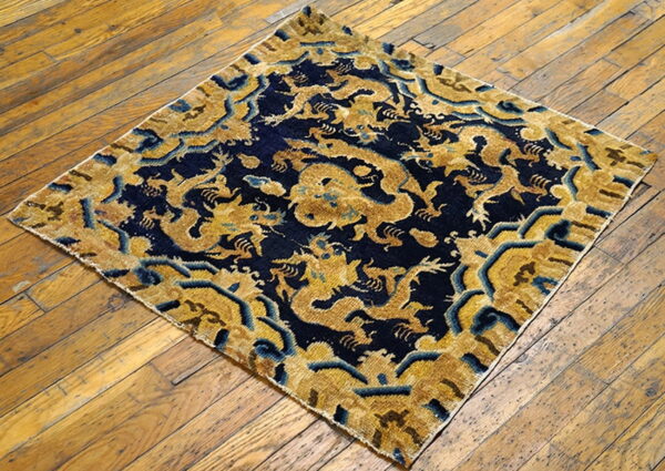 Low-pile square rug featuring gold dragons on a dark blue ground, set on aged wood flooring.