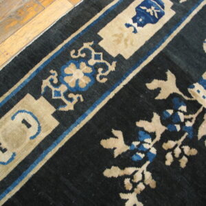 Dark blue rug with beige and royal blue ornate scrollwork lies partially covering light wood plank flooring.