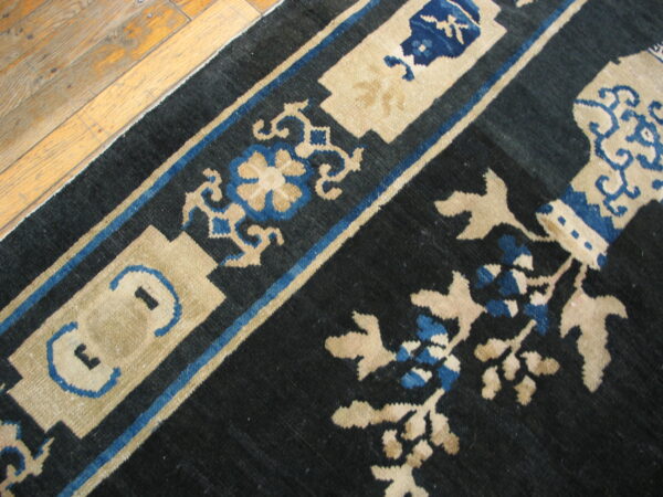 Dark blue rug with beige and royal blue ornate scrollwork lies partially covering light wood plank flooring.