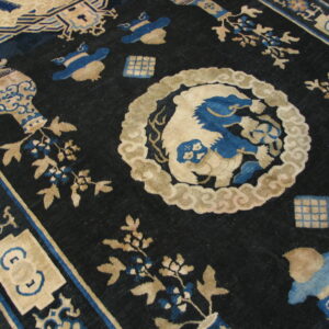 Ornate indigo rug featuring tan and blue mythological creatures, vases, and floral elements on a dark field.
