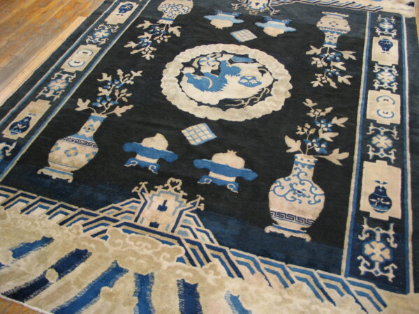 Dark blue rug featuring beige and light blue vases, foliage, and a detailed medallion on wood flooring.
