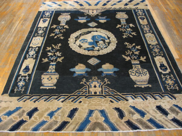 Navy blue and beige traditional rug featuring vases, scrolls, and a central mythical animal motif on wood floors.