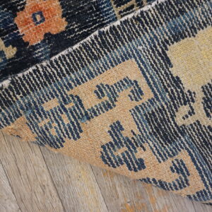A dark blue and orange patterned rug is partially rolled back on weathered gray wood flooring.