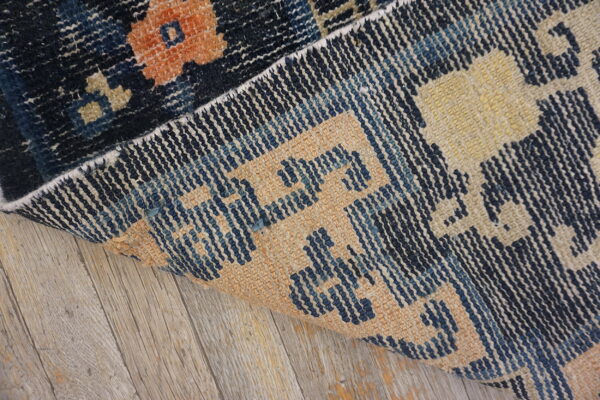 A dark blue and orange patterned rug is partially rolled back on weathered gray wood flooring.