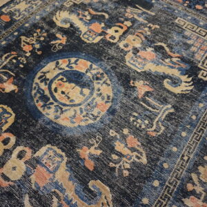 Low-pile navy rug featuring a faded tan medallion and geometric border on wood flooring.