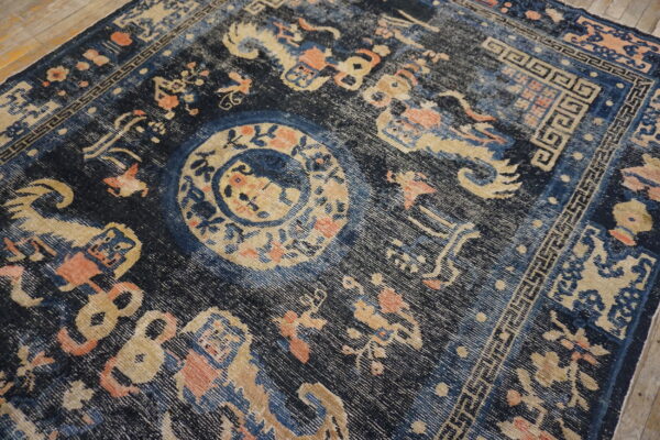 Low-pile navy rug featuring a faded tan medallion and geometric border on wood flooring.
