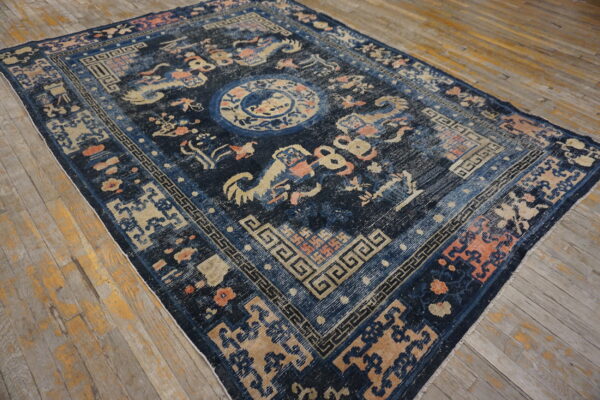 Distressed navy rug featuring beige and coral ornate designs, key borders, and a central medallion on wood floors.
