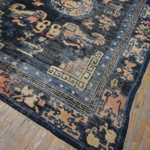 Dark blue rug with gold, peach, and light blue pattern detail rests on distressed wood floorboards.