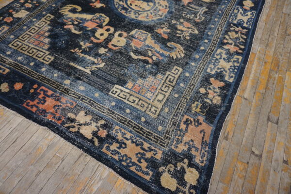 Dark blue rug with gold, peach, and light blue pattern detail rests on distressed wood floorboards.