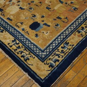 Close-up of a mustard yellow rug featuring stylized blue patterns and a thick navy border on exposed wood flooring.