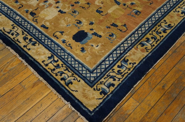 Close-up of a mustard yellow rug featuring stylized blue patterns and a thick navy border on exposed wood flooring.