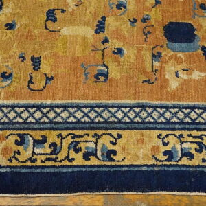Saffron and navy patterned rug detail showing a geometric and scrolling border next to a low-pile field.