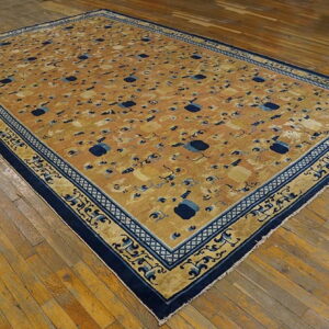An ochre rug featuring a repeating cloud pattern and elaborate blue and gold borders sits on hardwood.