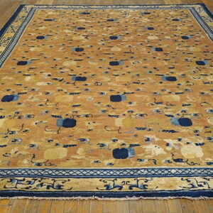 Large golden rug with scattered dark blue patterns and detailed borders rests on wooden flooring.