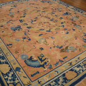 Traditional rug in pink, navy blue, and tan featuring scattered stylized figures on wood floor.