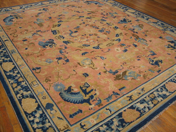 Traditional rug in pink, navy blue, and tan featuring scattered stylized figures on wood floor.