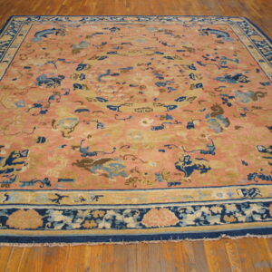 A low-pile salmon rug featuring blue stylized dragons and tan motifs covers wooden plank flooring.
