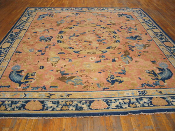 A low-pile salmon rug featuring blue stylized dragons and tan motifs covers wooden plank flooring.