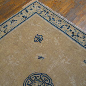 Tan rug with navy and light blue traditional patterns rests on aged hardwood planks.