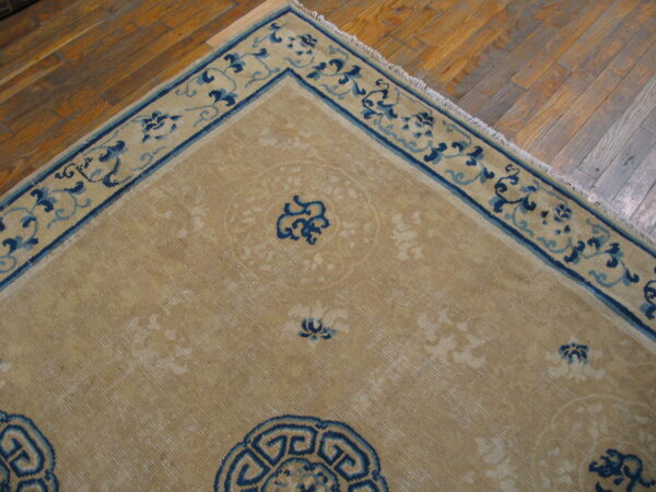 Tan rug with navy and light blue traditional patterns rests on aged hardwood planks.