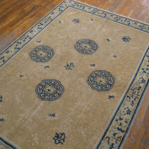 Beige rug with deep blue geometric medallions and a floral border rests on a wooden floor.