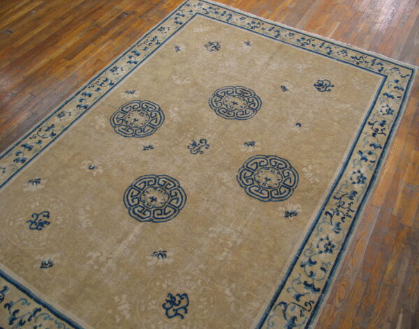 Beige rug with deep blue geometric medallions and a floral border rests on a wooden floor.