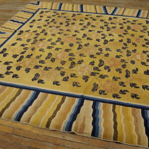 Yellow rug with scattered blue botanical motifs and a multi-colored wavy striped border on wood flooring.