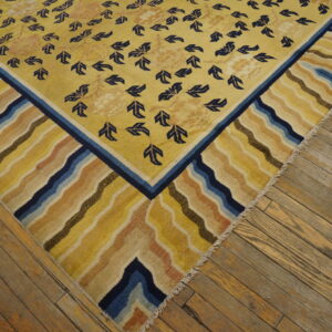 Golden yellow rug with navy foliage pattern and a wide, multicolored wavy border on distressed wood floors.