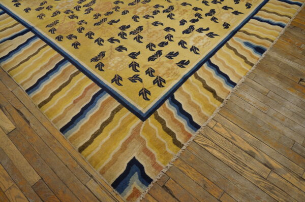 Golden yellow rug with navy foliage pattern and a wide, multicolored wavy border on distressed wood floors.