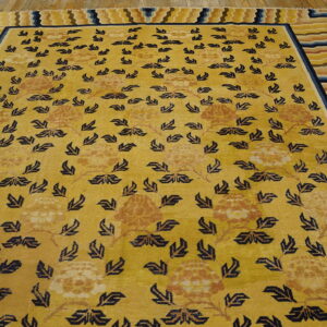 Golden yellow rug with dark blue floral patterns and a multi-colored striped border on wood flooring.