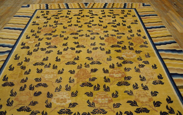 Golden yellow rug with dark blue floral patterns and a multi-colored striped border on wood flooring.