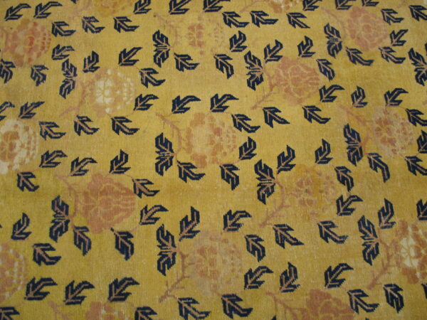 Gold rug with a dense pattern of dark blue stylized leaves and large subtle orange floral designs.