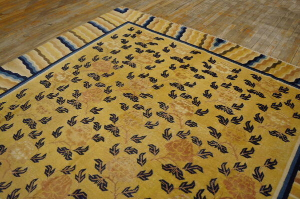 Gold rug featuring navy leaves, faded florals, and a wavy striped border rests on worn wood flooring.