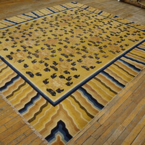 Golden yellow rug with blue foliage and a striped wavy border lays diagonally on light brown wood flooring.