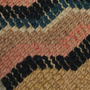 Close-up of a textured rug featuring diagonal stripes in black, blue, pink, cream, and tan.