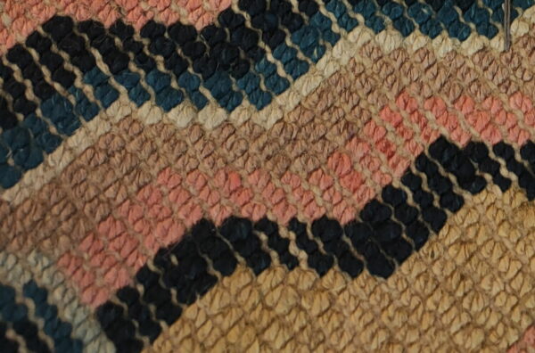 Close-up of a textured rug featuring diagonal stripes in black, blue, pink, cream, and tan.