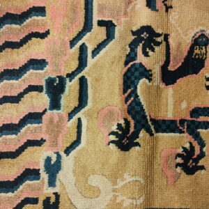 A close view of a textured rug with stylized designs in tan, dark blue, pink, and cream.
