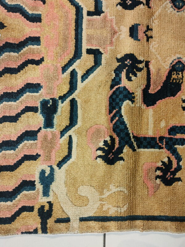 A close view of a textured rug with stylized designs in tan, dark blue, pink, and cream.