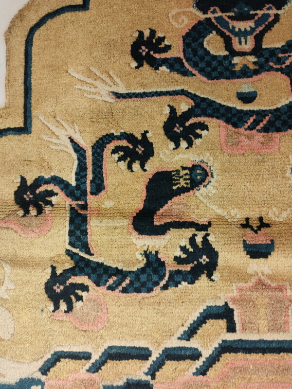 Detail view of a beige rug featuring a dark blue and pink stylized dragon and cloud pattern.