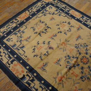 Tan rug with floral and bird motifs, featuring a navy border, on distressed wood flooring.