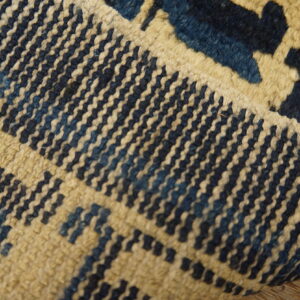 Textured blue and cream rug with geometric patterns is partially folded on rustic wood planks.