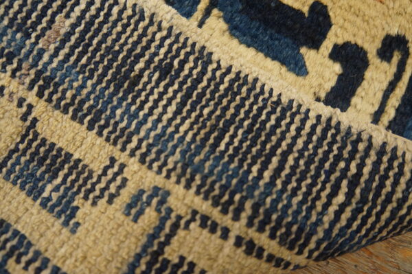 Antique chinese - ningxia small scatter size wool blue rug 2 Textured blue and cream rug with geometric patterns is partially folded on rustic wood planks.