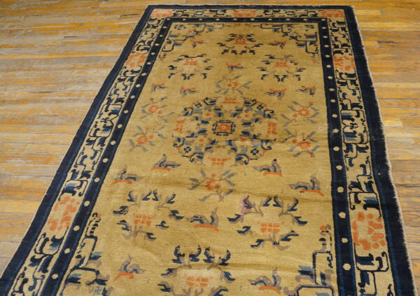 Antique chinese - ningxia small scatter size wool blue rug 3 Muted gold rug with stylized blue and coral accents and a dark border lies on distressed wooden flooring.