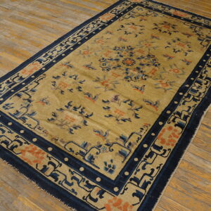 Tan and orange floral rug with thick navy blue geometric borders lying on wide-plank wood floor.