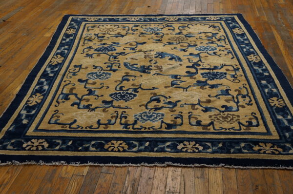 Stylized gold and blue floral rug with a thick border over distressed hardwood flooring.