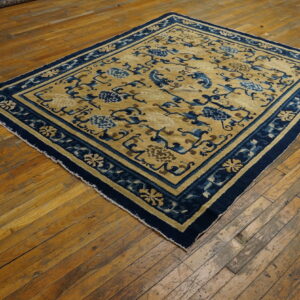 Gold and navy rug with stylized floral patterns lies on distressed wood floors.