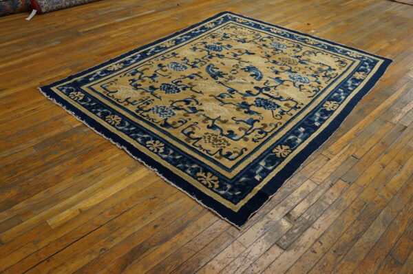 Gold and navy rug with stylized floral patterns lies on distressed wood floors.